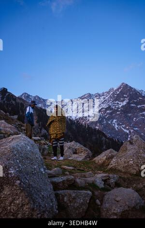 Due escursionisti avvolti da coperte si stagliano su un sentiero di montagna durante il crepuscolo a Triund, Mcleodganj, Himachal Pradesh, India. Foto Stock