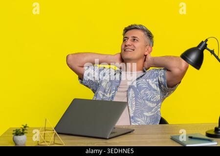 Un uomo di mezza età si è concentrato mentre scriveva sul laptop a tavola, mostrando determinazione e sforzo mentale, quindi si piega tranquillamente indietro in sollievo. Young Guy ha finito il progetto e si è rilassato isolato su sfondo giallo Foto Stock