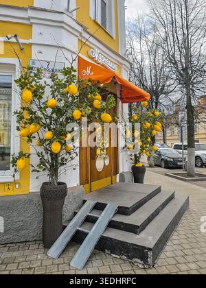 Gatchina, Russia - 06 aprile 2026: Ristorante italiano Marcellis a Gatchina. Facciata gialla luminosa con tenda arancione e porta in legno. I limoni adornano due alti alberi decorativi in vasi tessuti scuri. Scalini in calcestruzzo conducono all'ingresso, fiancheggiati da rampe metalliche. Vert Foto Stock