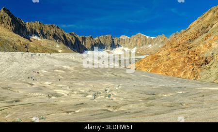 Rhonegletscher, Svizzera - 06.09.2025: Ampio paesaggio del massiccio Ghiacciaio del Rodano con piccoli escursionisti che navigano sulla sua superficie ghiacciata nelle Alpi. Foto Stock