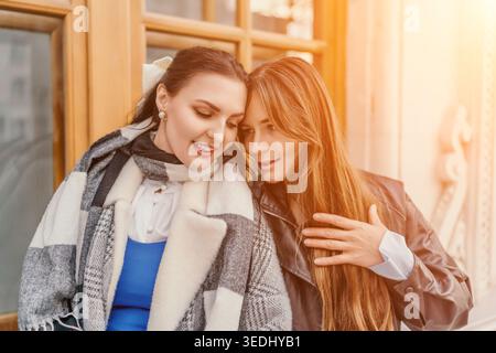 Amici e donne sorridenti condividono un momento di gioia all'aperto alla luce del sole autunnale indossando cappotti e sciarpe eleganti Foto Stock