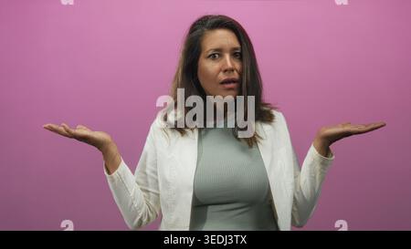 La donna alza mani e tira le mani con i palmi in uno studio sullo sfondo rosa, la bocca leggermente aperta e guarda in avanti; confusione. Foto Stock