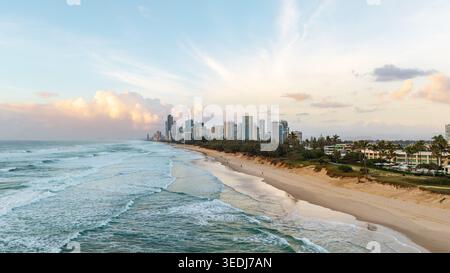 Una vista aerea dello skyline della Gold Coast che si estende lungo una spiaggia sabbiosa, dove le dolci onde si incontrano con la moderna e alta architettura durante un sereno tramonto. Foto Stock
