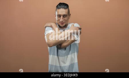 Uomo con mani allungate che si avvicina in avanti e sorride in studio con camicia a righe e sfondo pesca; comfort abbraccia l'apertura. Foto Stock