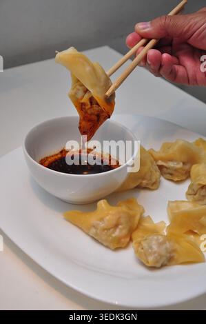 Wonton al vapore con olio di peperoncino servito in un piatto bianco sopra un tavolo bianco Foto Stock