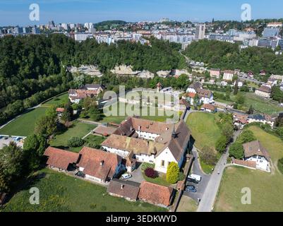 Vista aerea del Monastere de Montorge con edifici storici in pietra con tetti di tegole rosse, prati verdi lussureggianti e lo skyline urbano sotto un'aria limpida Foto Stock