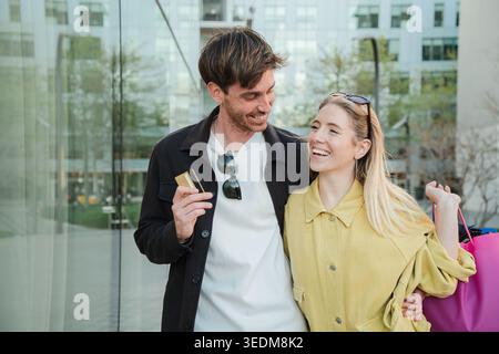 Una coppia gioiosa condivide un momento delizioso insieme mentre fanno acquisti, tenendo in mano una carta di credito e sorridendo calorosamente l'uno con l'altro, esprimendo la loro felicità Foto Stock
