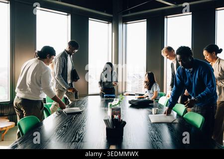 Un gruppo di diversi colleghi si riuniscono attorno a un lungo tavolo nero per una riunione in ufficio Foto Stock