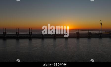 Vista aerea della barriera di Deltawerken con una turbina eolica durante un tramonto dorato sul Mare del Nord. Foto Stock