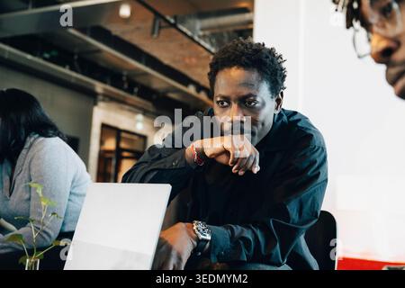 Imprenditore concentrato che guarda un notebook mentre è seduto accanto a un collega che lavora in ufficio Foto Stock