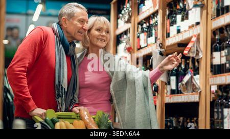 Coppia che fa shopping insieme in un negozio di alimentari, selezionando bottiglie di vino durante la serata Foto Stock