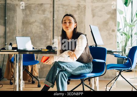 Ritratto di un uomo d'affari che tiene il telefono seduto sulla sedia in ufficio Foto Stock