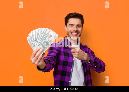 Young Man tiene i soldi mentre sorride su uno sfondo arancione in un ambiente casual Foto Stock