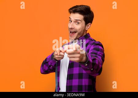 L'uomo posa e punta la fotocamera davanti a uno sfondo arancione durante un momento casuale Foto Stock