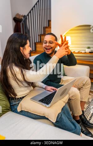Coppia felice e variegata che celebra il successo lavorando da casa Foto Stock