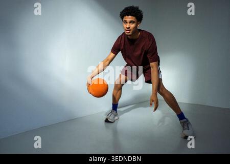 Ritratto a figura intera giovane che pratica abilità di basket vicino al muro Foto Stock