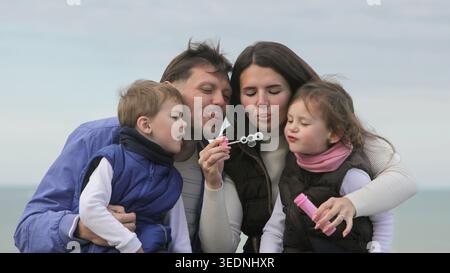 Genitori e bambini si divertono con la famiglia insieme a bolle di sapone all'aperto in un parco in una giornata d'autunno nuvolosa. Foto Stock