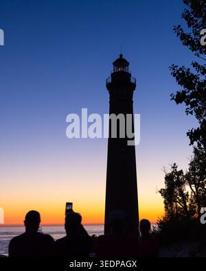 Sagome di persone che guardano il faro di Big Sable Point con un cielo vibrante al tramonto Foto Stock