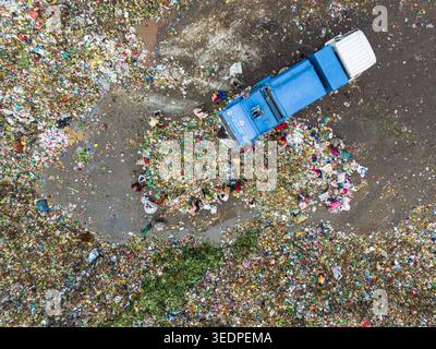Aminbazar, Bangladesh - 26 gennaio 2025: Veduta aerea dei raccoglitori di rifiuti che smistano tra pile di rifiuti colorati di plastica accanto a un camion della spazzatura blu a. Foto Stock