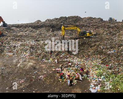 Aminbazar, Bangladesh - 26 gennaio 2025: Veduta aerea della discarica di Aminbazar con escavatori che trasportano rifiuti e persone che scavano attraverso pali di gar Foto Stock