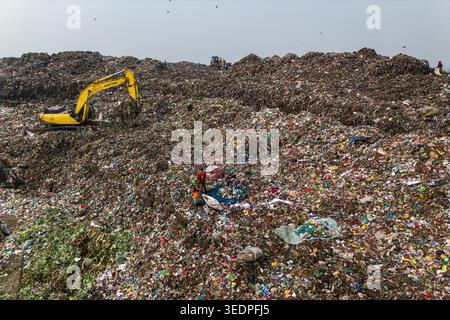 Aminbazar, Bangladesh - 26 gennaio 2025: Veduta aerea della discarica di Aminbazar con un escavatore giallo che sposta i rifiuti e le persone che scavano attraverso il cumulo Foto Stock
