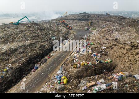Aminbazar, Bangladesh - 26 gennaio 2025: Veduta aerea dell'enorme discarica di Aminbazar con escavatori e camion che trasportano rifiuti lungo una strada sterrata sottostante Foto Stock
