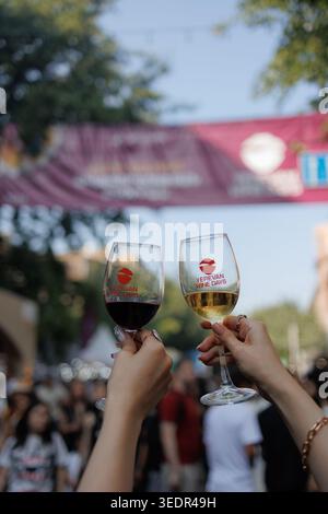 I visitatori del Festival del vino di Yerevan tengono i bicchieri di vino rosso e bianco davanti allo striscione del festival l'8 giugno 2025 a Yerevan, Armenia. Foto Stock
