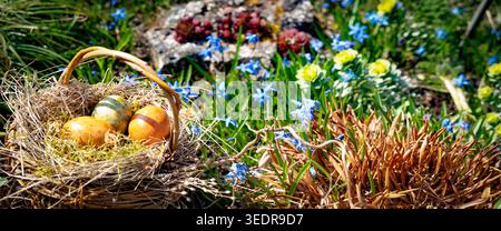 Cestino di salice fatto in casa con uova di pasqua in un prato primaverile con fiori colorati. Foto Stock