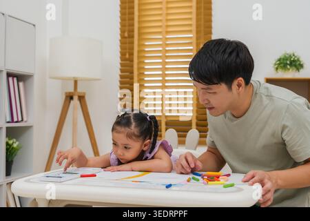 padre e bambina disegnano e dipingono con colori pastello ad olio su carta a casa Foto Stock