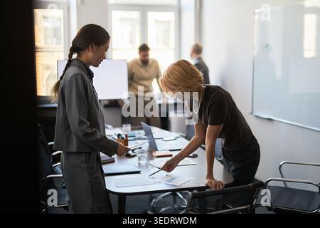 Donne d'affari che esaminano documenti e discutono strategie durante la riunione d'ufficio, presentano lavoro di squadra e pianificazione. Utile per la comunicazione aziendale, la leadership, la consulenza Foto Stock