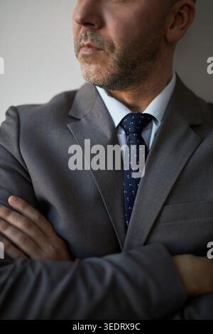 Ripresa verticale di un uomo d'affari adulto in piedi con le braccia incrociate, guardando lontano, che trasmette fiducia e leadership. Adatto per il branding aziendale e la messaggistica gestionale Foto Stock