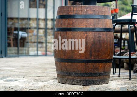Una botte di legno sorge accanto a un caffè a Skopje, nella Macedonia del Nord, con sedie nelle vicinanze alla luce del giorno. Foto Stock