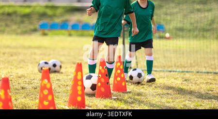 Giocatori di calcio giovanile che praticano esercizi di agilità con coni arancioni e palloni multipli sul campo erba - sessione di allenamento Junior per il controllo della palla e. Foto Stock