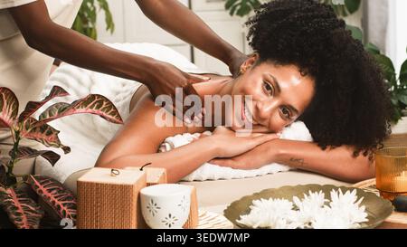 Sessione di massaggio rilassante nella Spa: Donna sorridente che riceve un trattamento per collo e spalle in un ambiente di benessere sereno Foto Stock