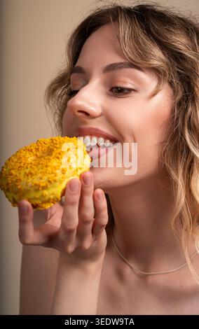 Donna che gusta una dolce ciambella gialla, un gustoso dessert per spuntini e festeggia la felicità Foto Stock
