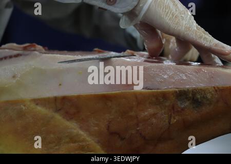 Primo piano di uno chef professionista che affetta un prosciutto italiano intero con un coltello affilato per fare fette sottili e delicate Foto Stock