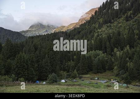 Aire de bivouac (TMB), Francia - 11.09.2025: Una vista panoramica delle colorate tende da campeggio annidate in una valle verde circondata da foreste e vette alpine u Foto Stock