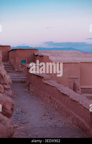 Ait Benhaddou, Marocco: Stretto sentiero di terra tra antiche mura di argilla rossa della fortezza di ksar al crepuscolo. Spazio di copia sfondo viaggio. Foto Stock