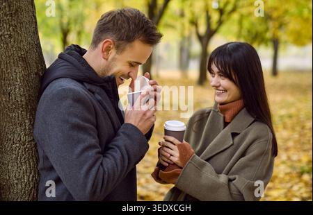 Coppia felice che beve caffè nel parco autunnale, condividendo calore e benessere mentale Foto Stock