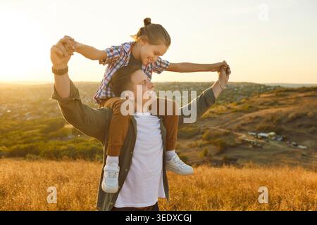 Padre e figlio felici che si divertono insieme al tramonto, bambini che cavalcano sulle spalle Foto Stock