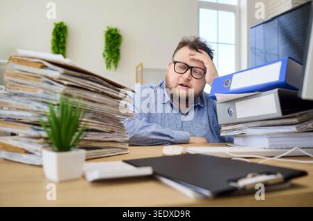 Lavoratore d'ufficio stressato sopraffatto da documenti cartacei, fatica e scadenze imminenti Foto Stock