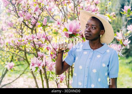 Giovane donna africana in cappello di paglia tra i fiori di magnolia rosa in Spring Garden Foto Stock