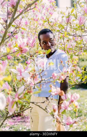 Giovane donna africana che guarda attraverso i rami di Magnolia nel Sunny Spring Park Foto Stock