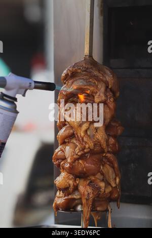 Sfrigolante carne di shawarma di pollo arrostito su arrosto verticale sputare presso l'autentico mercato asiatico di strada. Preparazione professionale del kebab donatore. Foto Stock