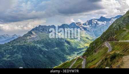 Timmelsjochstrasse, sulla strada per Merano, una strada tortuosa si snoda attraverso un verde paesaggio alpino montagnoso sotto un cielo nuvoloso Foto Stock