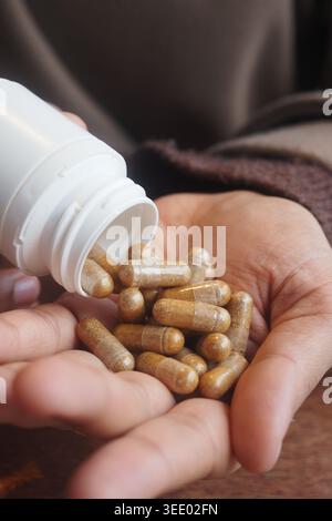 Le capsule versano dalla bottiglia alla mano aperta su un tavolo di legno Foto Stock