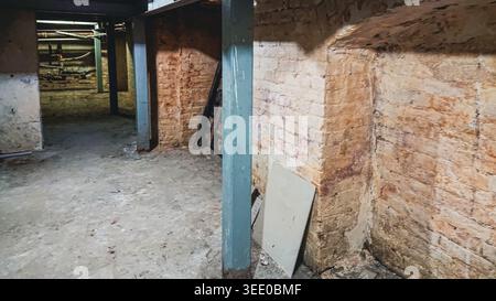 Vista ravvicinata dei lavori di rinforzo strutturale nel seminterrato di un vecchio edificio, evidenziando le pareti in mattoni e le travi di supporto Foto Stock