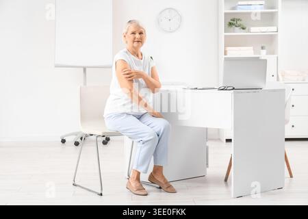 Donna anziana con cerotto medico dopo la vaccinazione seduta in clinica Foto Stock