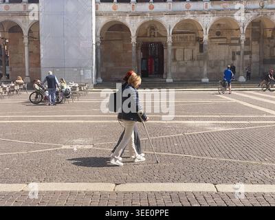 Cremona, Italia 9 aprile 2026 donna adulta con stampella che cammina attraverso la storica piazza acciottolata di Cremona, Italia, mostrando mobilità, determinazione, a Foto Stock