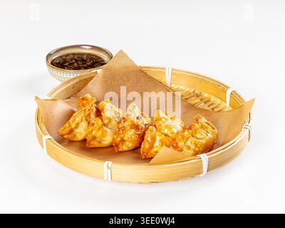 Appetitoso cibo asiatico. Gnocchi fritti dorati croccanti serviti in una vaporiera di bambù con salsa di soia scura. Composizione minimalista con luminoso, cle Foto Stock